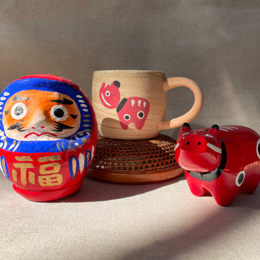 Akabeko handmade Fukushima Iwaki Japan Mug next to a Drama and an Akabeko. Akabeko is a traditional Japanese folk toy crafted in Aizu Japan.